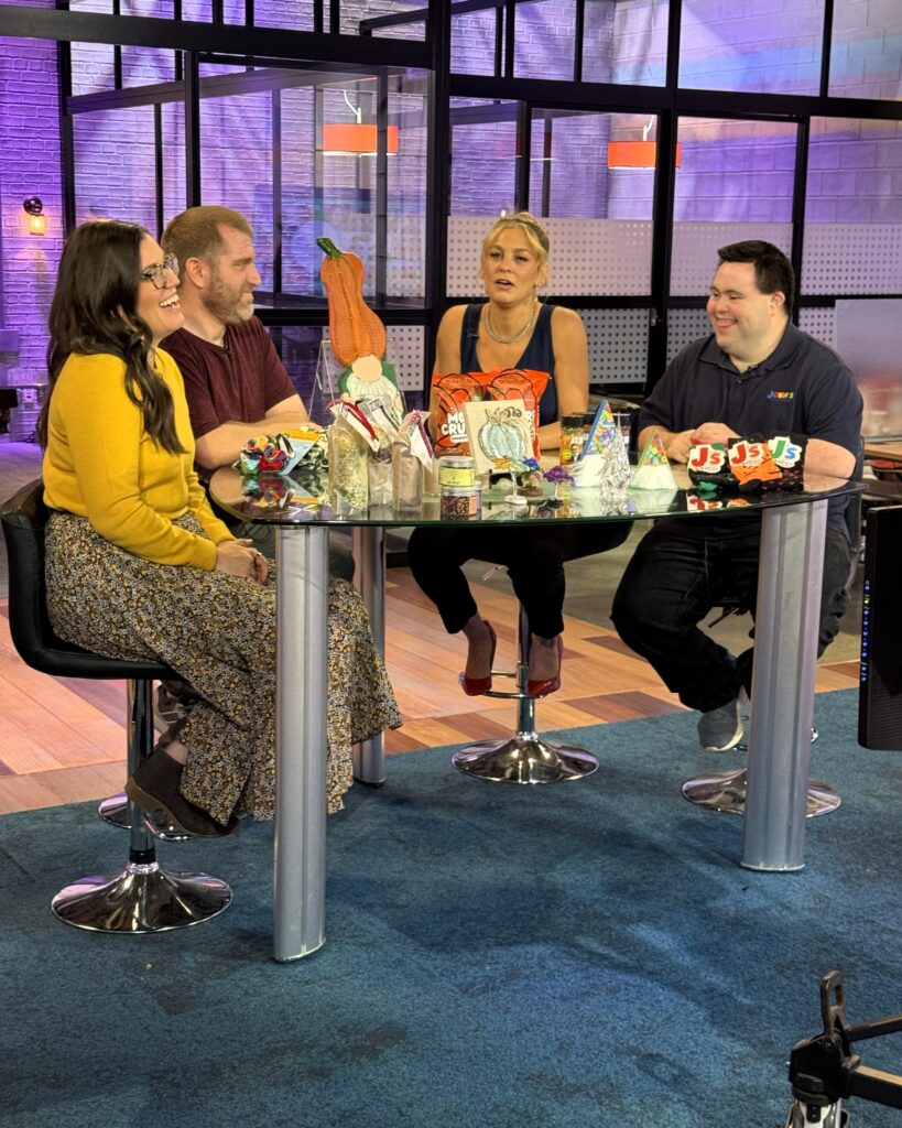 Four people, two womena nd two men incuidng JOhn at a table on the TV set of Colorado and COmpany